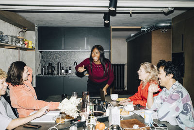 Cheerful female entrepreneur gesturing while coworkers sitting at table in creative office