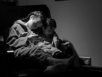 Girl with brother sitting on sofa while using mobile phone in darkroom