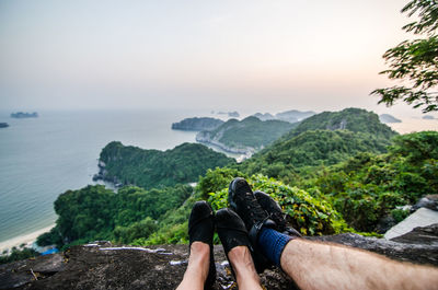 Low section of man on cliff by sea against sky