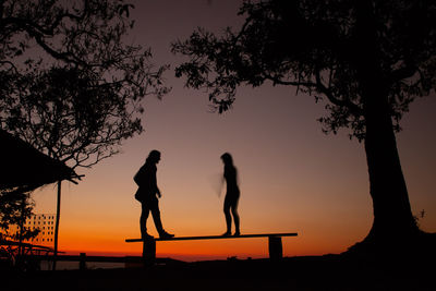 Silhouette people standing by tree against sky during sunset