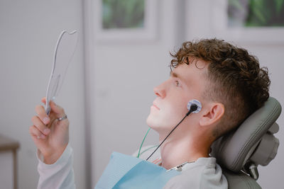 The patient sits in an orthodontist's chair during the tens procedure, looks in the mirror at the 