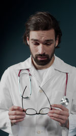 Doctor holding eyeglasses against blue background