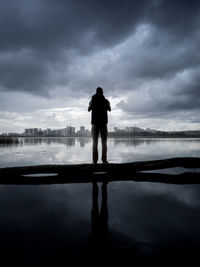 Rear view of silhouette man standing by lake against sky