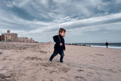 Happy young toddler running around the beach with a big branch