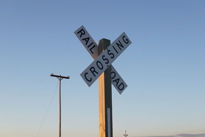 Railroad crossing sign against blue sky during sunset