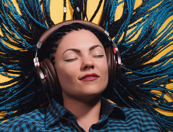 Close-up of young woman with braided hair listening to music against yellow background