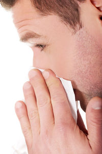 Close-up of man wiping nose with tissue against white background