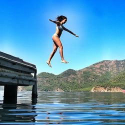 Full length of woman diving into lake against clear blue sky