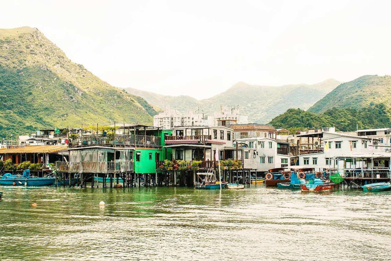 HOUSES BY RIVER AGAINST BUILDINGS AND MOUNTAINS