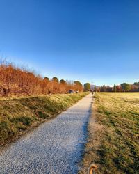 Surface level of road amidst field against clear blue sky