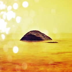 Close-up of rock in sea against sky during sunset