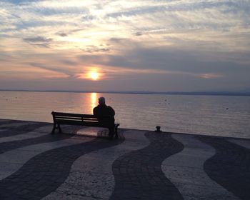 People sitting on bench looking at sea during sunset