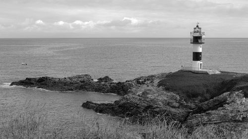 Lighthouse amidst sea and buildings against sky