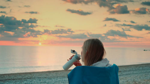 Woman photographing sea against sky during sunset
