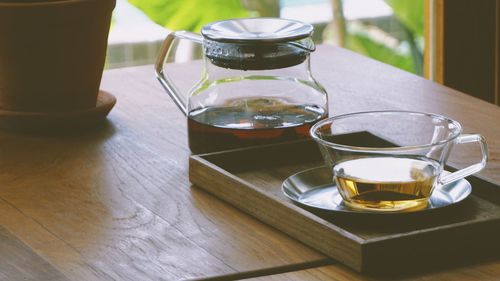 Close-up of glass tea pot and mug served on wooden table