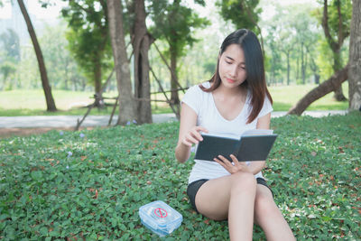 Young woman sitting in park against trees