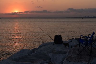 Fishing rod on rock by sea against sky during sunset