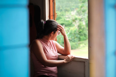 Woman looking away while sitting on window at home