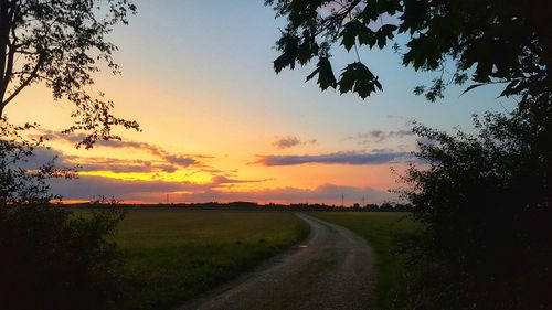 Road amidst field against sky during sunset