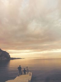 People on pier at sea against sky during sunset