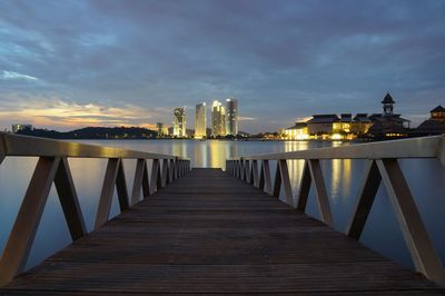 Bridge over river amidst buildings against sky at dusk