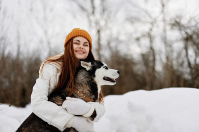 Smiling woman with dog on snow covered field