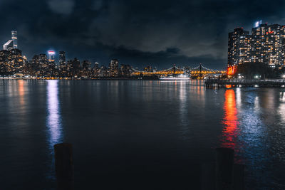 Illuminated buildings by river against sky at night