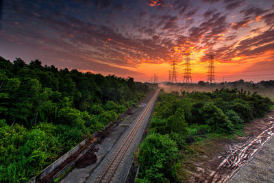 Railroad track amidst trees against sky during sunset