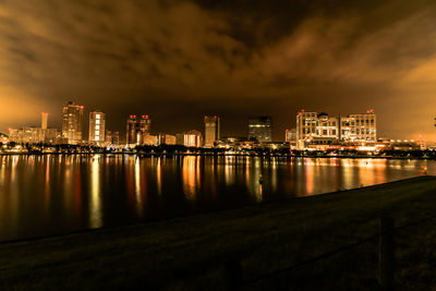 Illuminated buildings by river against sky at night