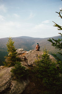 Rear view of woman sitting on rock against mountains