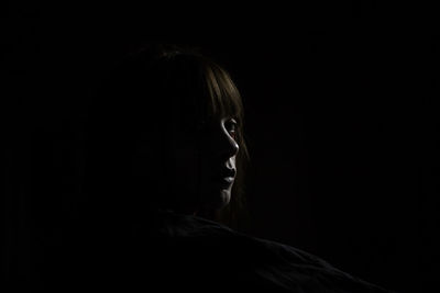 Close-up of young woman against black background