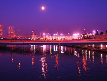 Illuminated city by sea against sky at night