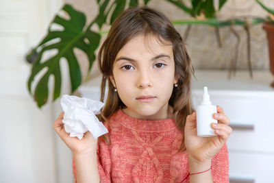 Portrait of sick girl with nasal spray and tissue sitting at home