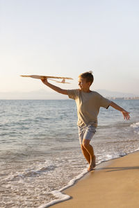 Rear view of woman jumping at beach against clear sky