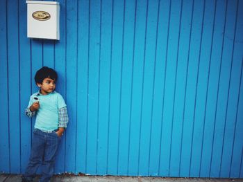 Boy with hand in pocket standing against blue wall