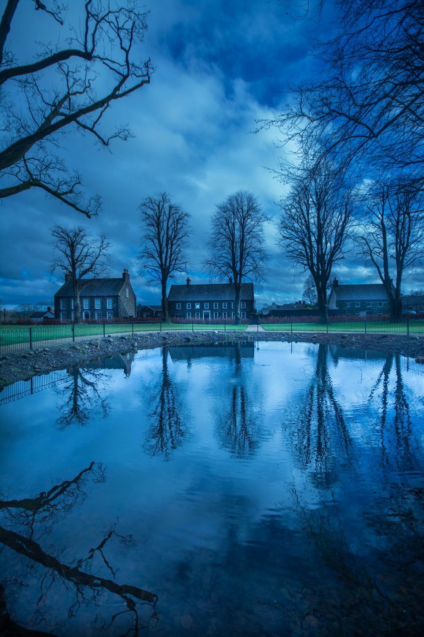 bare tree, architecture, water, built structure, sky, reflection, tree, building exterior, lake, cloud - sky, river, waterfront, cloud, tranquility, nature, tranquil scene, branch, outdoors, scenics, blue