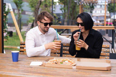 A guy and a girl are holding cocktails with a straw in their hands and eating pizza