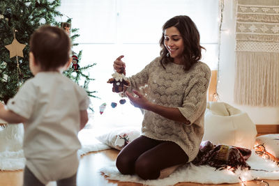 Mother playing with baby by christmas tree at home