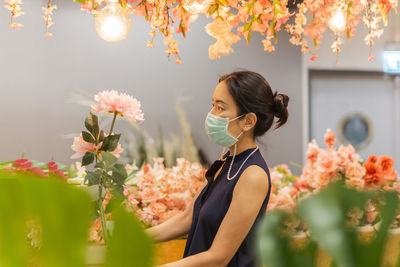 Woman in medicail mask chooses artificial flowers in flower shop