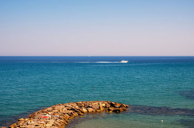 Rocky breakwater and boat on the sea horizon, liguria, italy