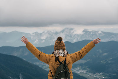 Back view of female hiker with outstretched arms, looking at amazing view in mountains in winter