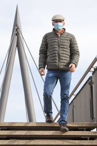 Mature man with face mask walking over a footbridge in a city - focus on the man