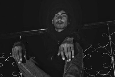 Portrait of young man looking away while sitting against black background