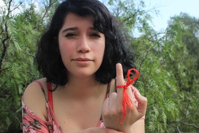 Close-up of young woman showing middle finger against plants