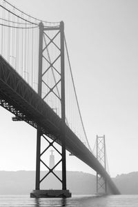 Low angle view of suspension bridge over sea against sky during foggy weather