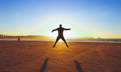 Rear view of man on beach against sky during sunset