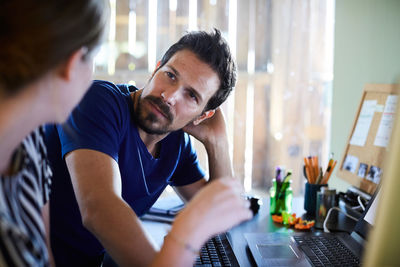 Businesswoman discussing with male colleague at computer desk in creative office