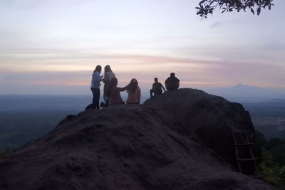 People standing on rock against sky during sunset