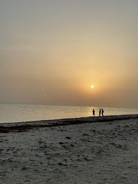 Silhouette people on beach against sky during sunset