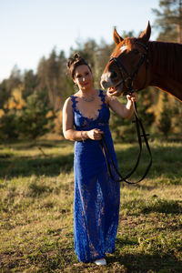 Full length portrait of woman standing by horse at forest